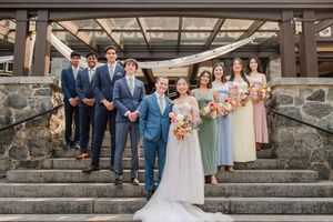 Wedding party in navy suits and pastel dresses pose together on rustic stone steps outdoors.