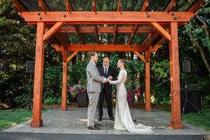 A wooden pergola in a garden creates a beautiful outdoor ceremony space with green foliage in the background.