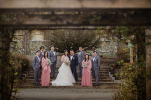 Wedding party poses on stone steps surrounded by greenery and old architecture.