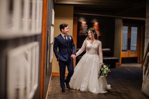 A bride and groom walk together through a covered walkway with wooden beams and natural lighting.