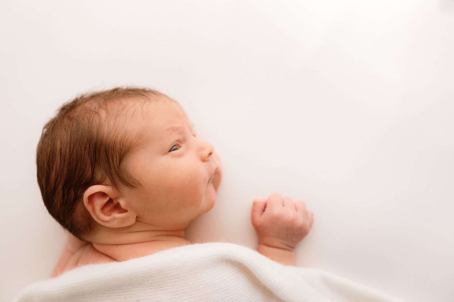 Sleeping newborn baby photographed in soft natural light against white background.