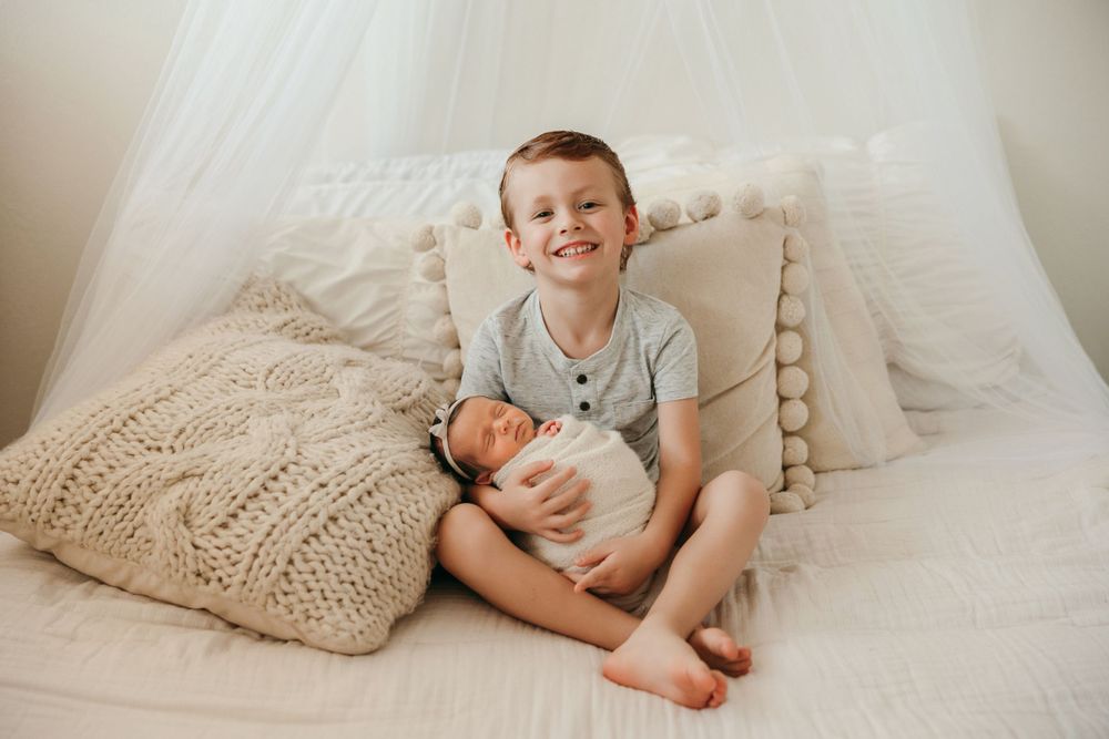 Two siblings sharing a sweet moment on a white bed with knit pillows.