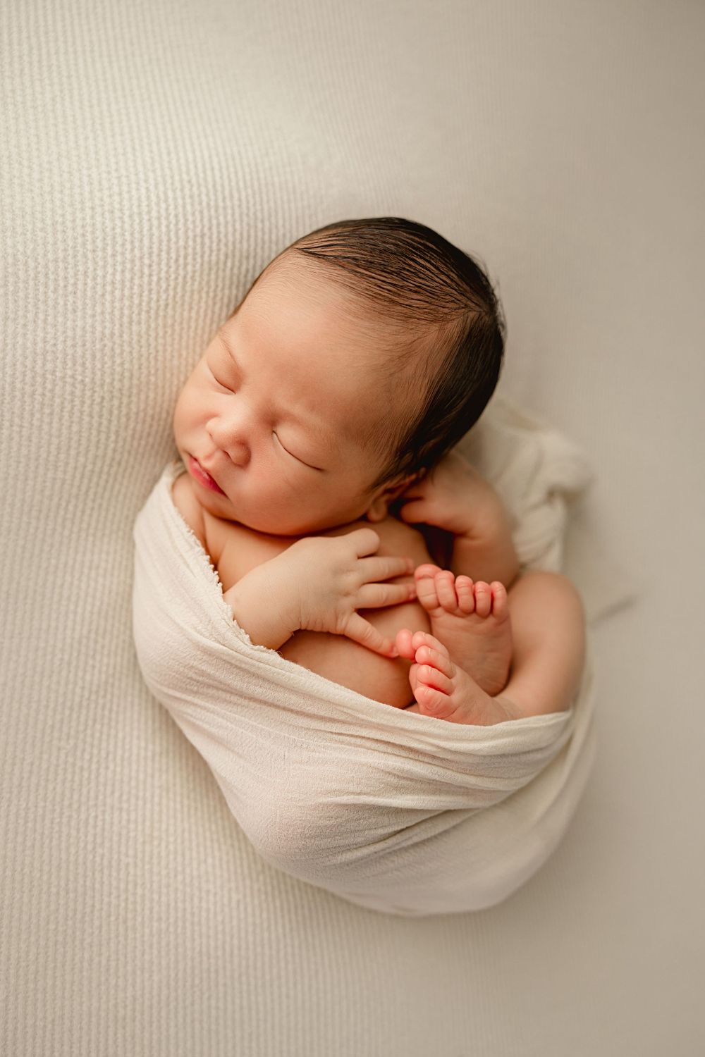 A sleeping newborn wrapped in white fabric on a textured background.