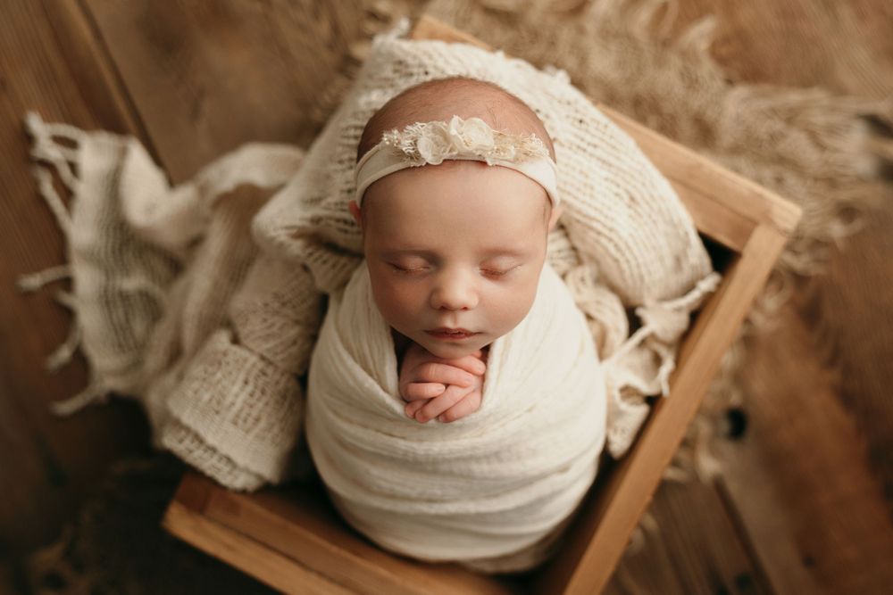 An overhead view of a sleeping newborn wrapped in cream fabric on a wooden surface.