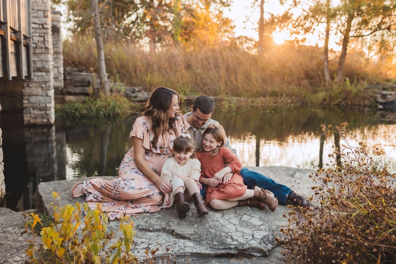 A family sits together with their white dog near a lake at sunset during autumn.