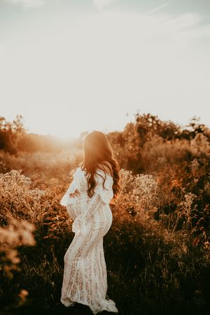 A dreamy golden hour portrait in a wildflower field with a white lace dress and flowing hair silhouetted against sunset light.