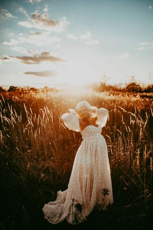 Two figures in white dresses stand together in a golden field at sunset creating a dreamy romantic scene.