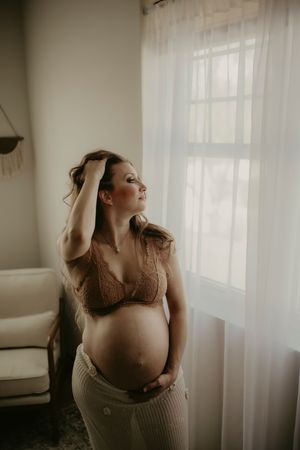 Artistic maternity photo series showing a pregnant woman in soft natural light by sheer curtains in a neutral setting.