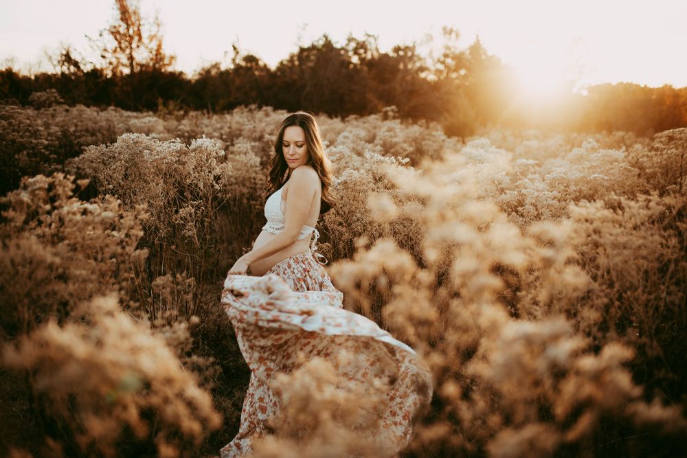 Golden hour maternity session in a field with flowing dress and dramatic sunlight.