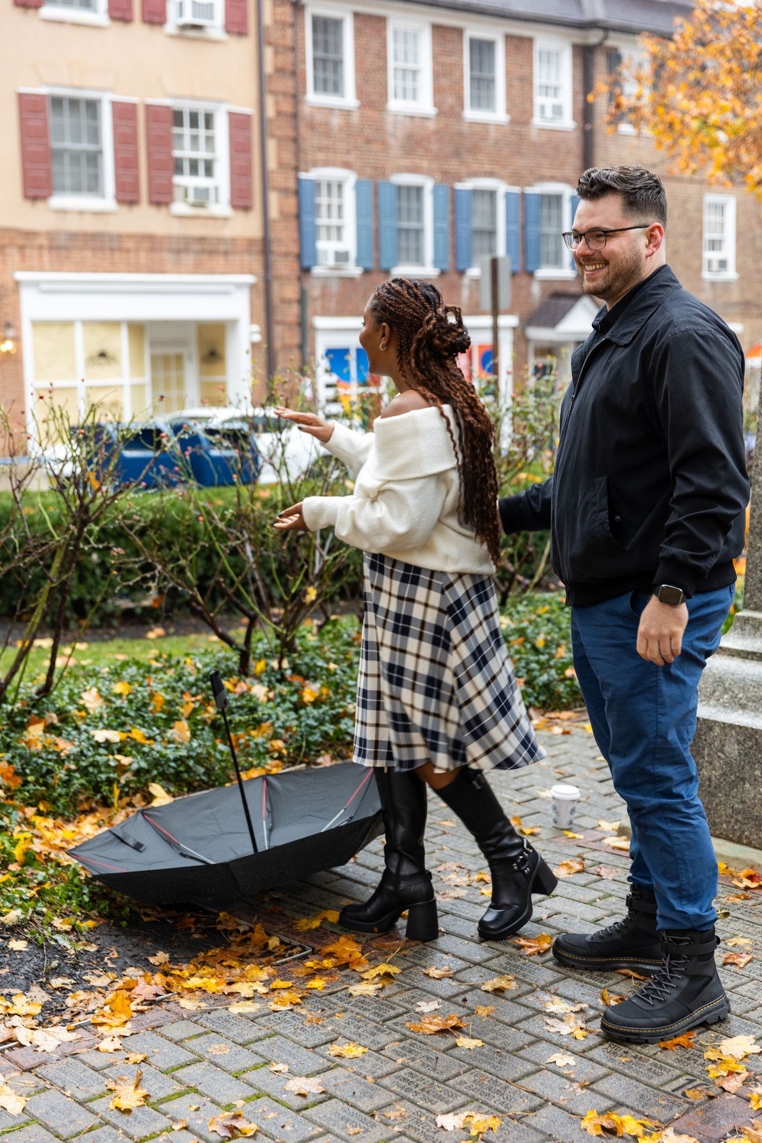 A couple walking on a brick sidewalk in autumn with fallen leaves and an umbrella during a romantic city stroll.