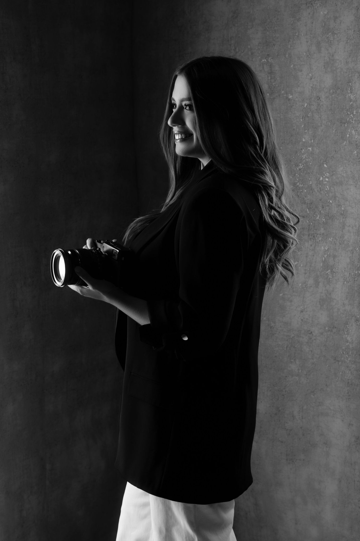 Moody black and white profile shot of a photographer holding camera against textured wall.