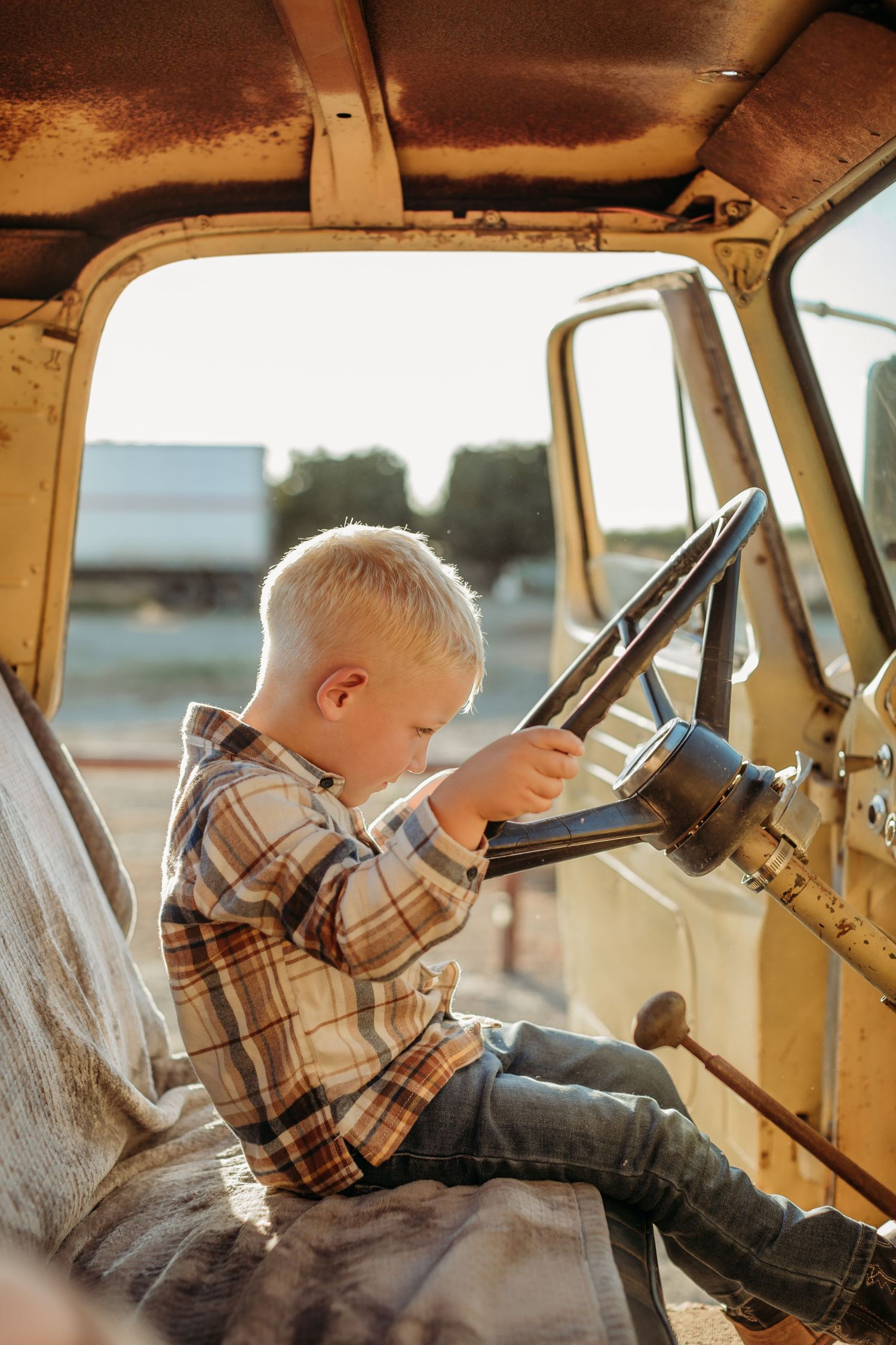A small child pretends to drive an old yellow truck while sitting in the driver's seat.