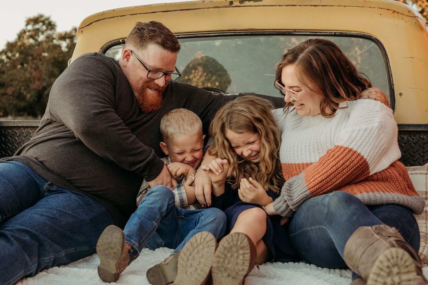 A family shares a joyful moment together while sitting in the bed of a vintage yellow truck.