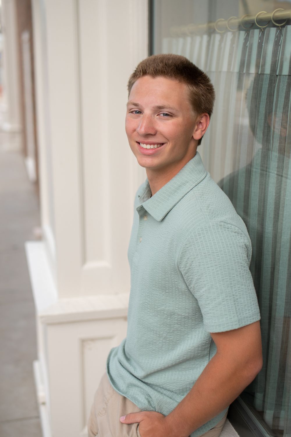 A person in a mint green polo shirt poses while sitting against a window in a series of four similar photos.