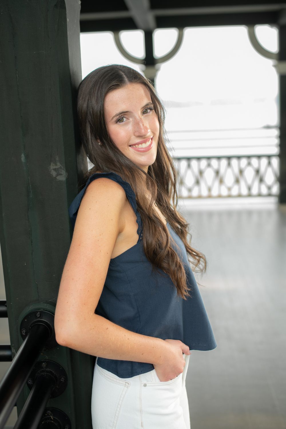 Woman in navy sleeveless top poses against railing in natural light setting.