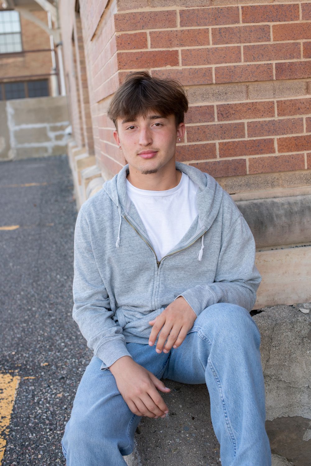 A person in a gray hoodie and jeans sits casually on brick steps in an outdoor setting.
