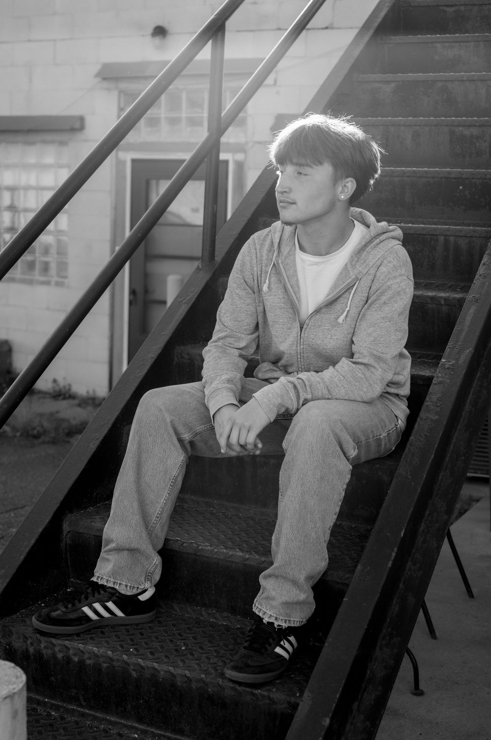 Black and white photo showing cropped views of someone sitting on dark steps wearing jeans and sneakers.