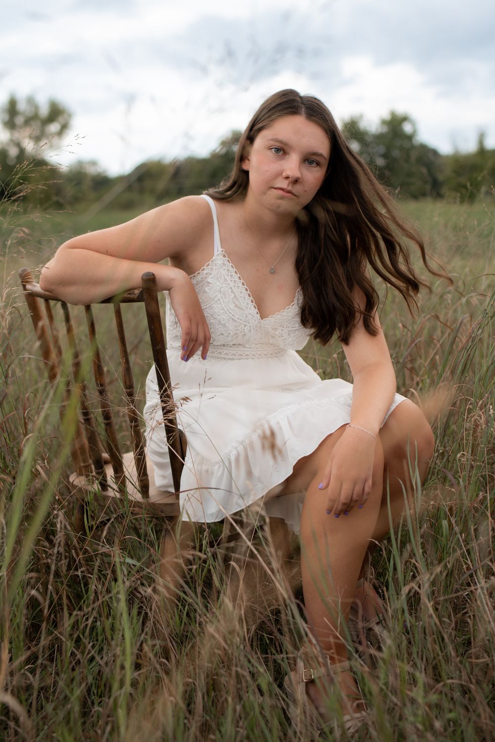 A person in a white lace dress poses gracefully in a field of tall grass during golden hour.