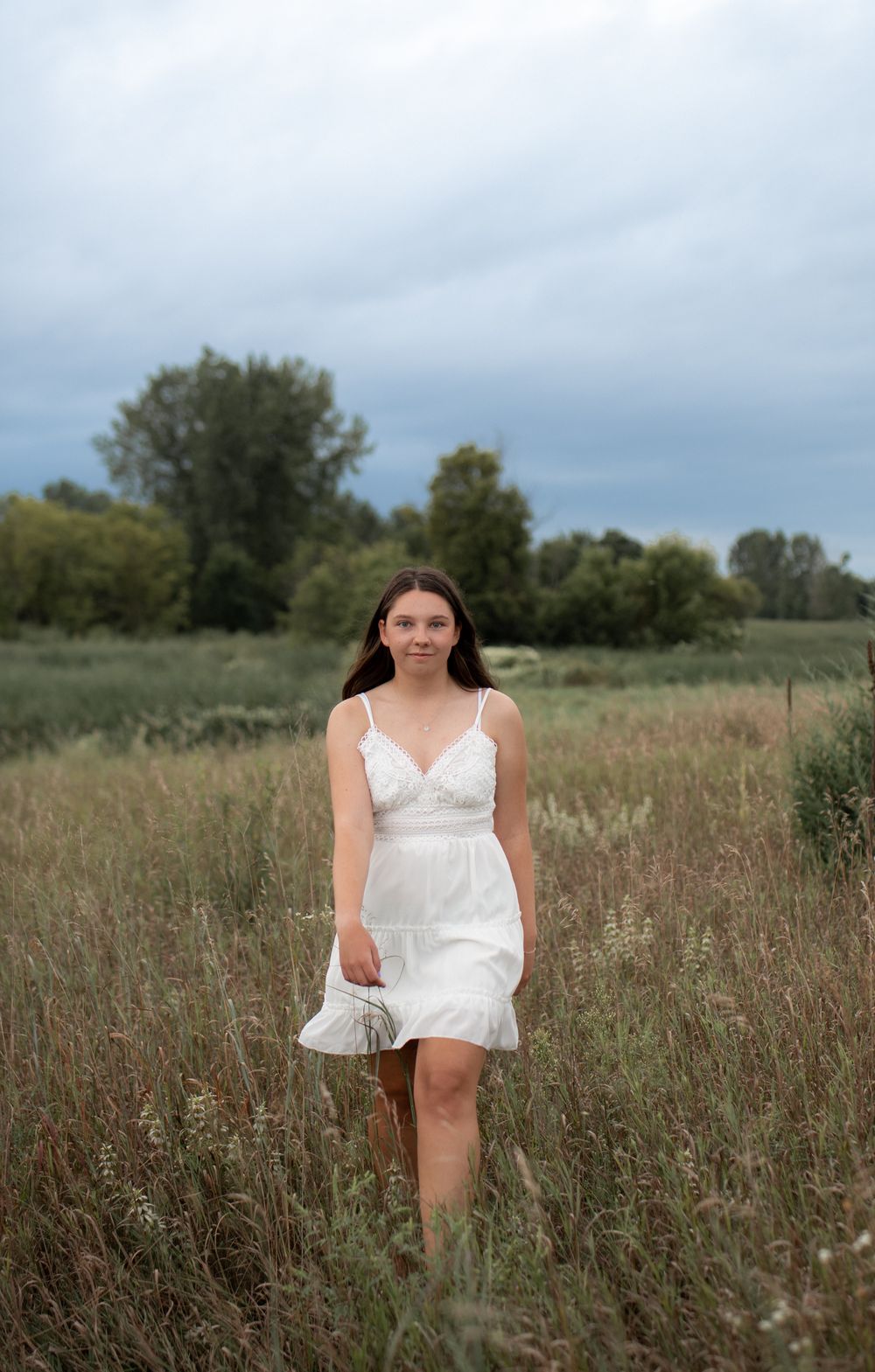 A white summer dress stands out against tall grass in a natural meadow setting.