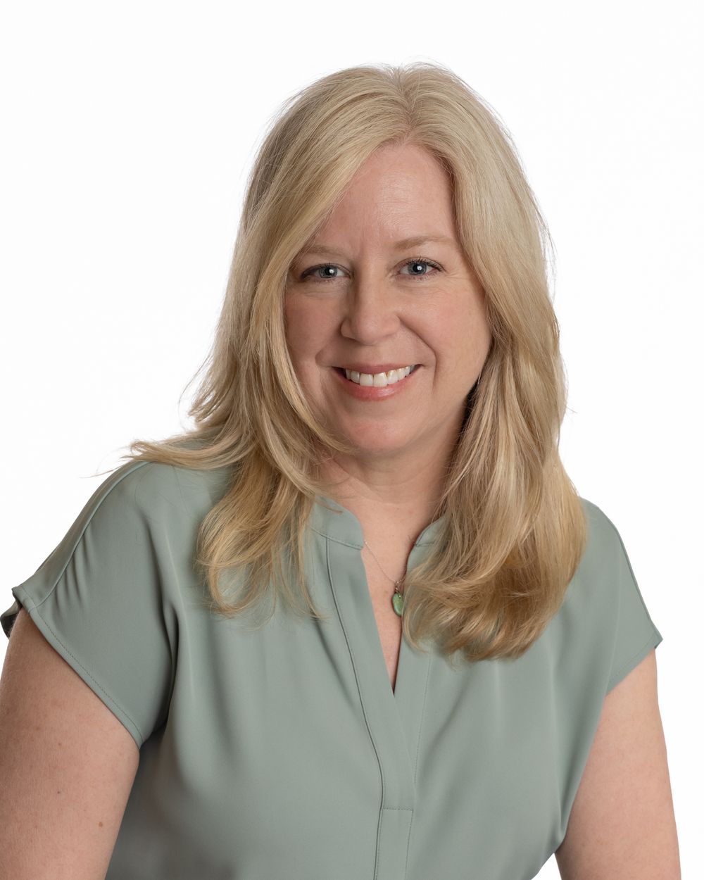 Professional headshot of smiling blonde woman in sage green blouse against white background.