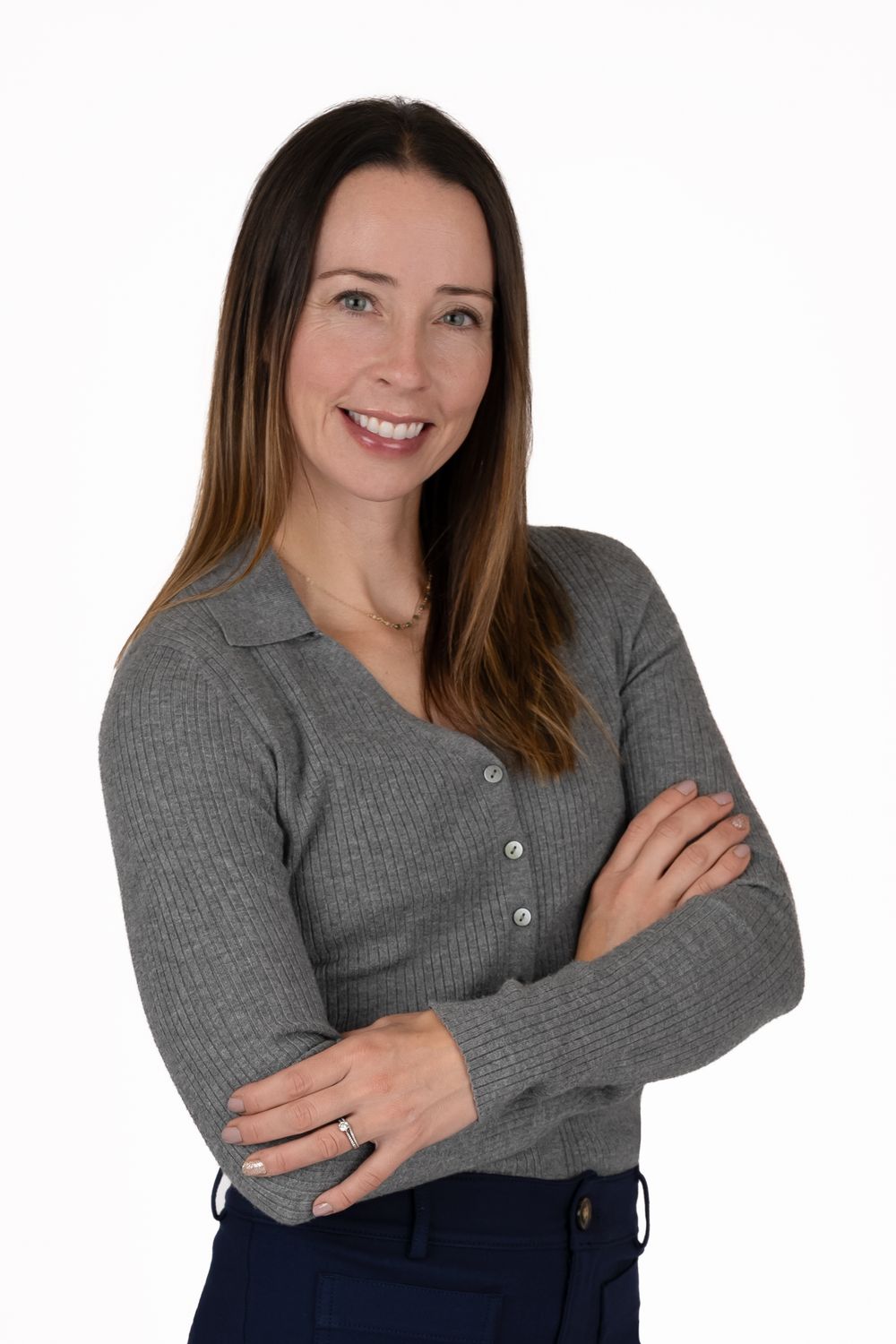 Professional woman in gray ribbed cardigan smiling with arms crossed against white background.