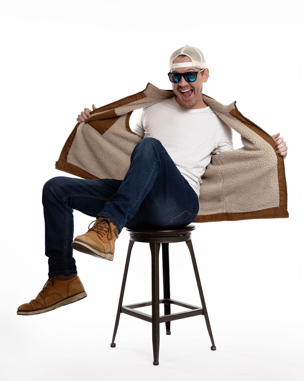 Smiling man in white tee and jeans showing sherpa-lined brown jacket interior while seated.