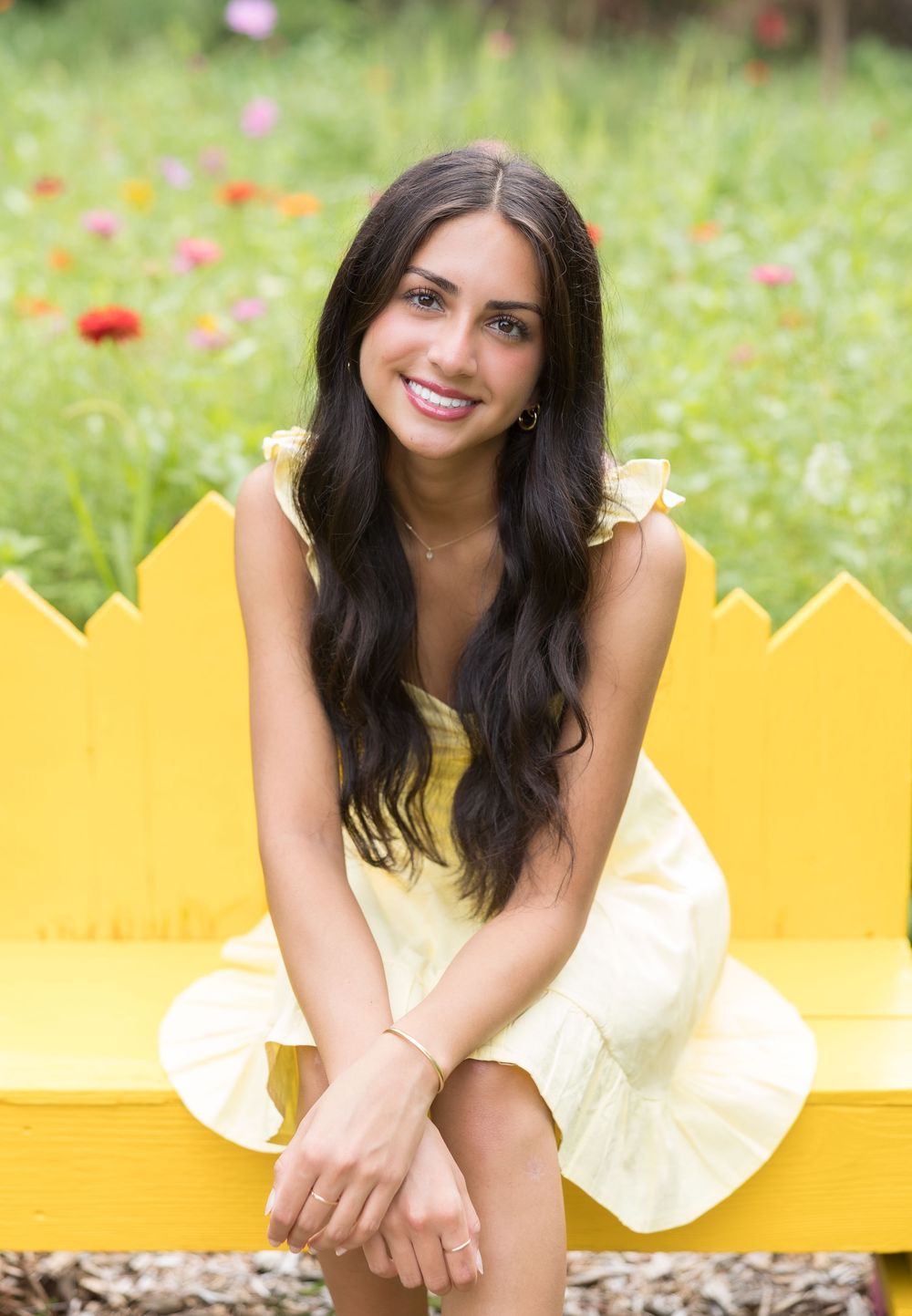 Young woman with long curly hair poses in a flowery meadow wearing a white dress.