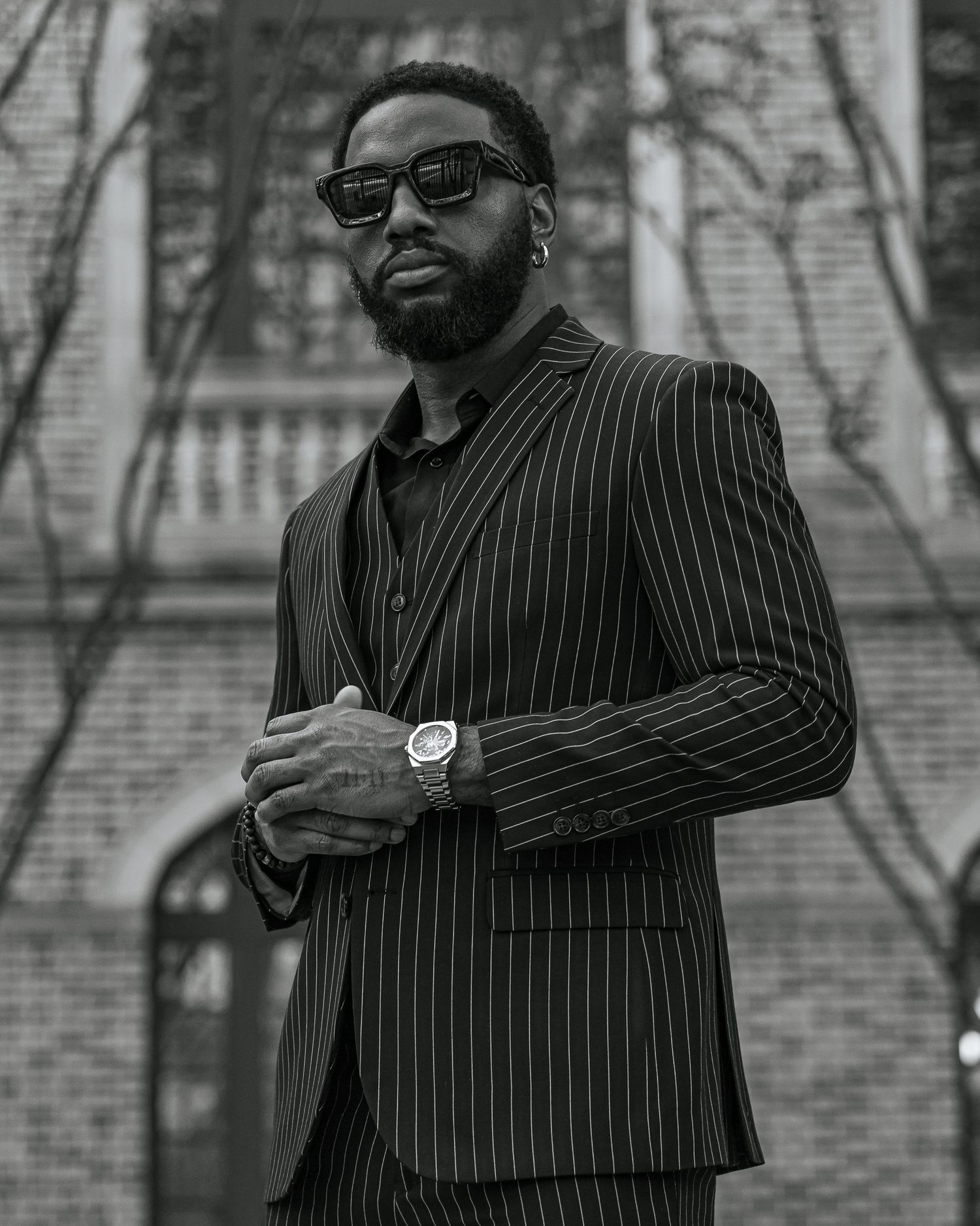 Stylish man in pinstriped suit posing confidently by wrought iron gate and brick building.