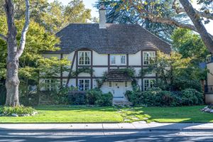 Tudor-style two-story home with half-timbered facade, shingled roof, and ivy-covered walls behind a manicured front lawn and mature trees.