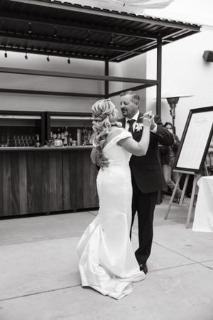 A couple shares their first dance in a venue with a rustic bar backdrop.