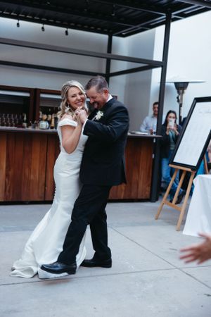 A couple dances and laughs together on an outdoor patio near a wooden bar.