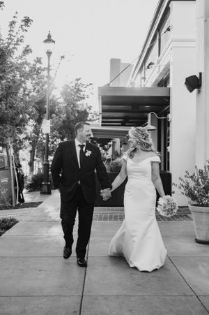 A couple walks hand in hand along a sidewalk with street lamps.