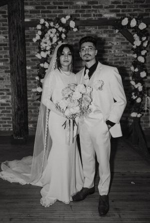 Wedding couple posing in front of a floral arch at a rustic brick venue.