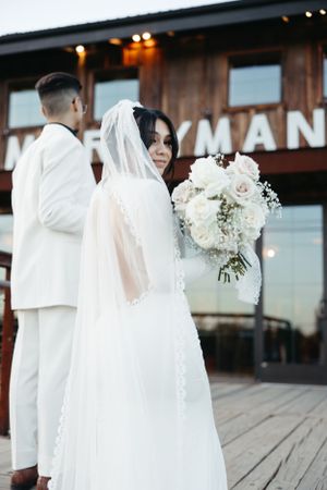 Bride holds white floral bouquet while posing outside Merryman Station.