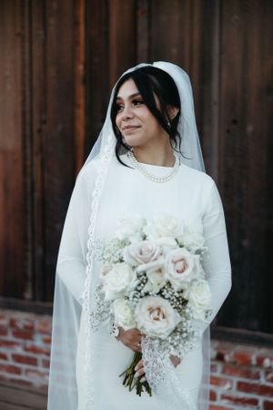 Bride in classic white wedding dress holding a bouquet of white roses and baby's breath.