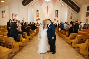 A wedding couple stands in a Catholic church aisle surrounded by wooden pews and pink bunting decorations.
