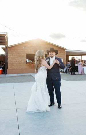 A couple dances at sunset outside a rustic wooden venue with string lights.