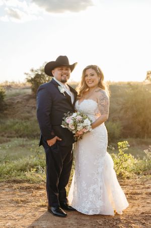 A western-themed wedding couple poses at sunset in a desert landscape with mountains.