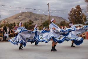 Dancers in flowing blue and white dresses perform at an outdoor wedding reception.