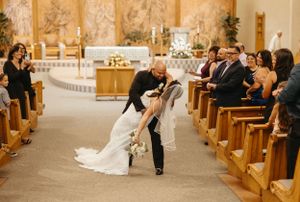 A romantic wedding kiss in a church aisle surrounded by wooden pews and elegant decor.