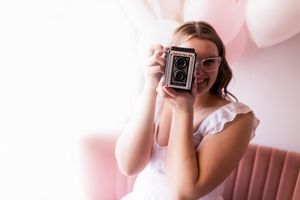 Person taking photos with a vintage camera against a pink background in a creative photography session.