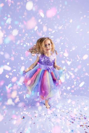 A magical scene shows a colorful tulle dress twirling amid pink and purple confetti against a dreamy pastel backdrop.