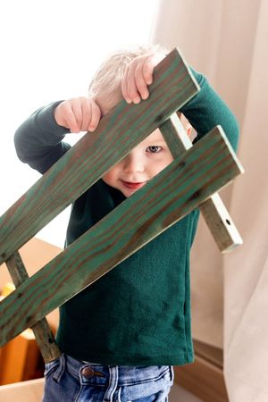 A playful moment peering through wooden slats of furniture while wearing a green sweater and jeans.