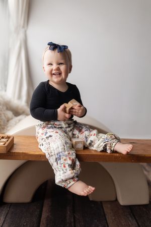 A series of four progressive photos showing a small child sitting and smiling on a wooden bench against a white wall.