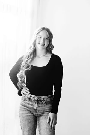 Woman in black top and jeans posing against white background.