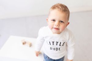 Baby in white shirt and gray pants photographed against white background.