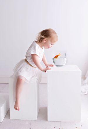 Child in white dress exploring white blocks in minimalist studio setting.