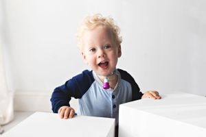 Young child in blue outfit playing and laughing against white backdrop.