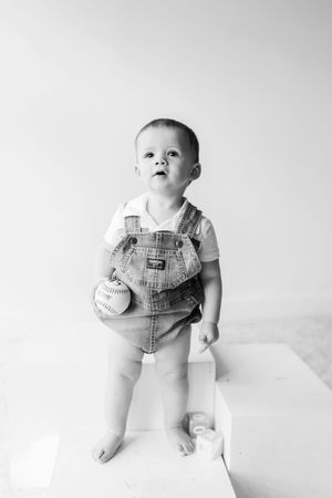 A series of black and white portraits showing an infant wearing denim overalls and white shirt against a light backdrop.