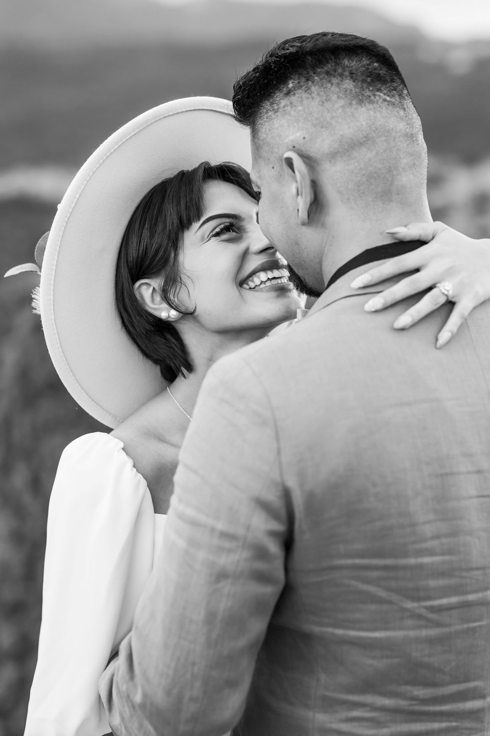 Intimate black and white portrait of wedding couple sharing tender moment with white hat detail.